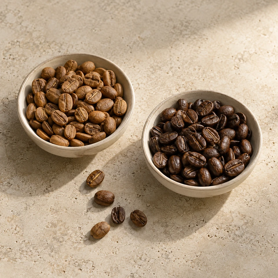 Two ceramic dishes holding lighter and darker roasted coffee beans side by side