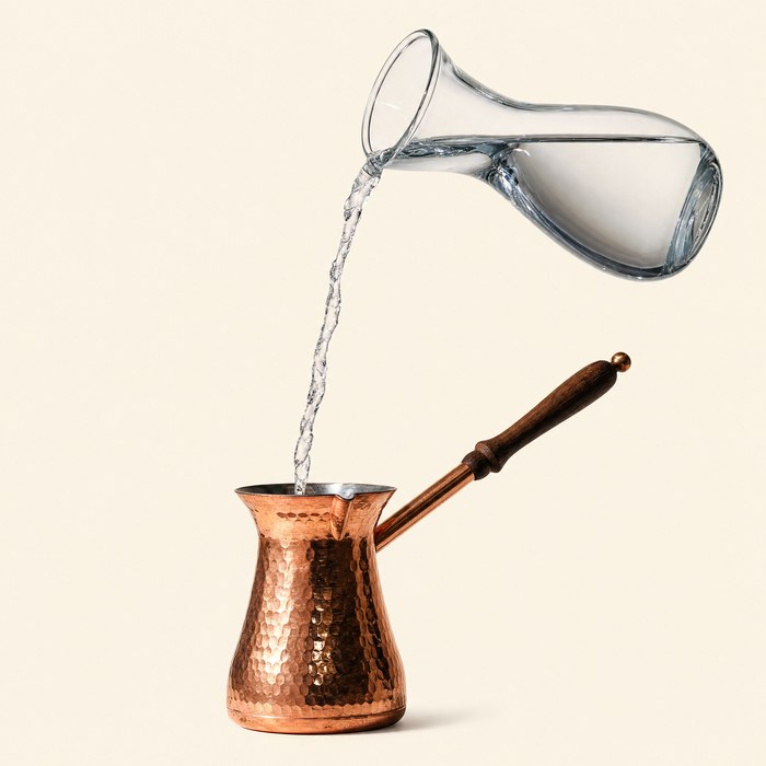 Cold water poured into a copper cezve on a warm cream ground