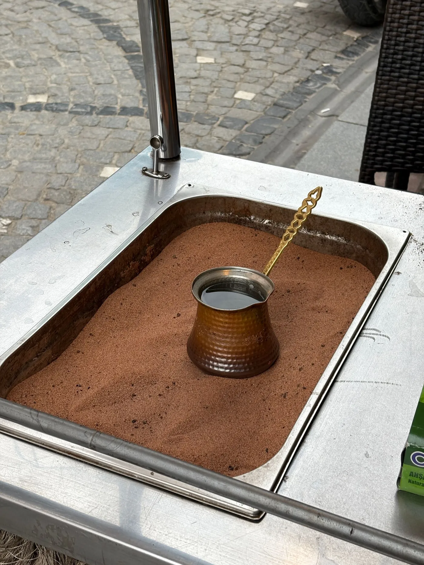 A copper cezve brewing in hot sand